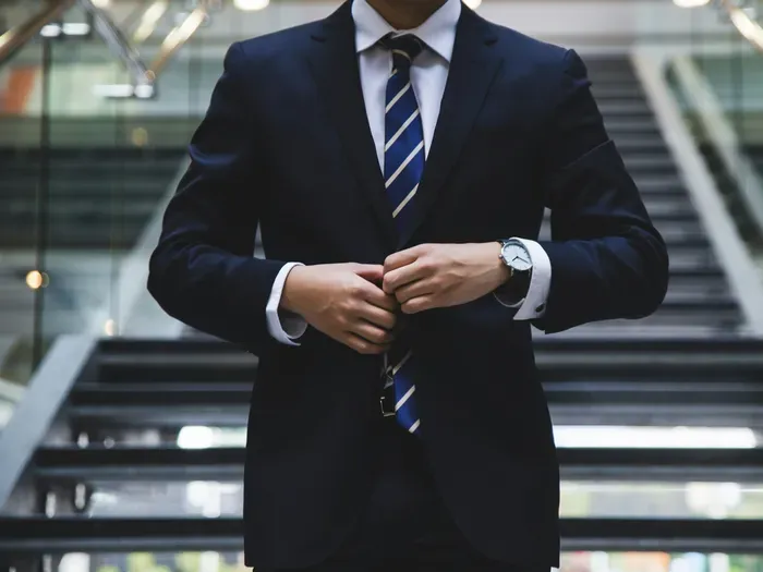 Confident businessman in navy suit adjusting his jacket while standing in a modern office staircase